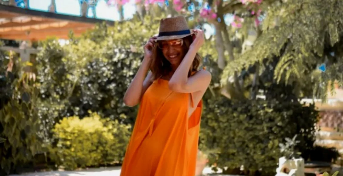 أمينة شلباية وهي ترتدي فستانا برتقاليا مع قبعة ونظارة شمس