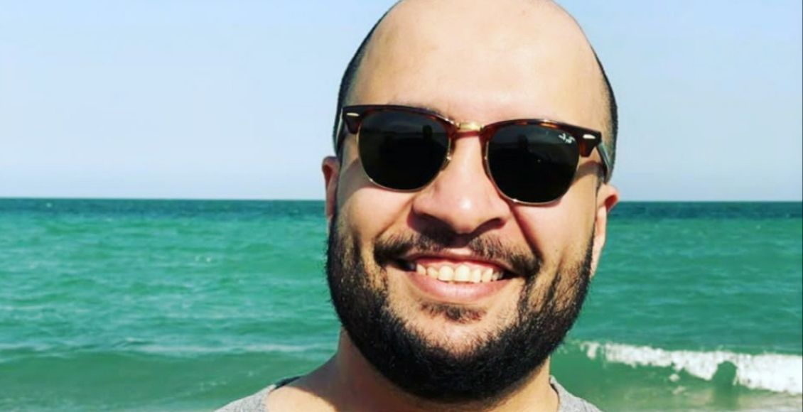 ابو عابد مرتديا نظارة شمسية على أحد الشواطئ وخلفه البحر.