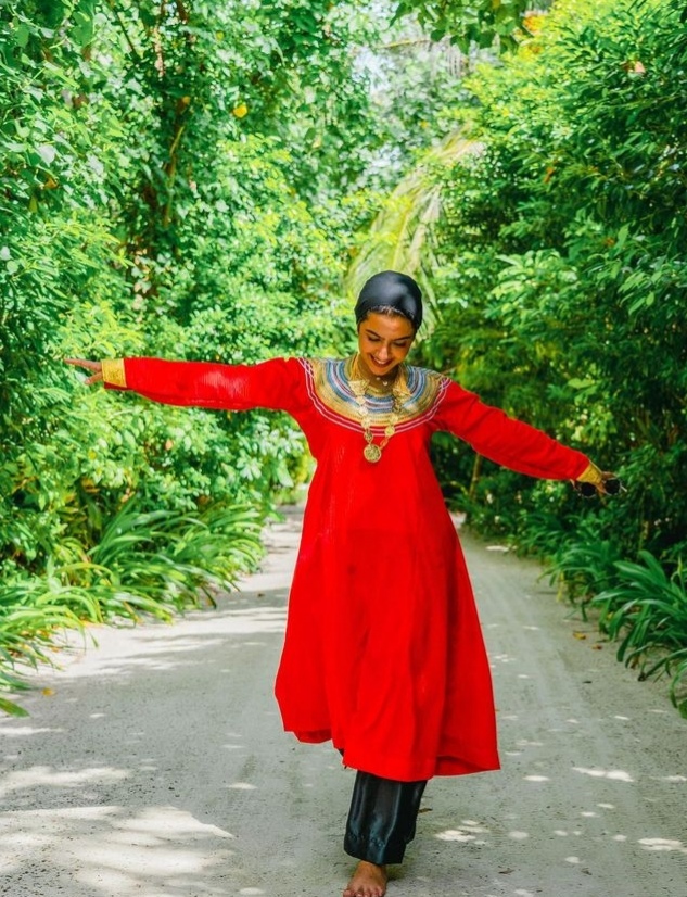 نجلاء الودعاني في جزر المالديف مرتدية الزي التقليدي وهو عبارة عن فستان أحمر ذو أكمام وتطريزة ذهبية على الصدر