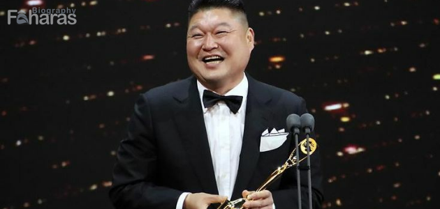 كانغ هو دونغ مرتديا بدلة رسمية ممسكا بجائزة